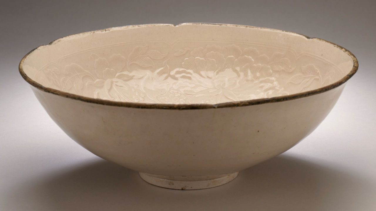 Cream-colored Chinese Ding ware bowl with floral carvings and a slightly scalloped rim, displayed against a neutral background
