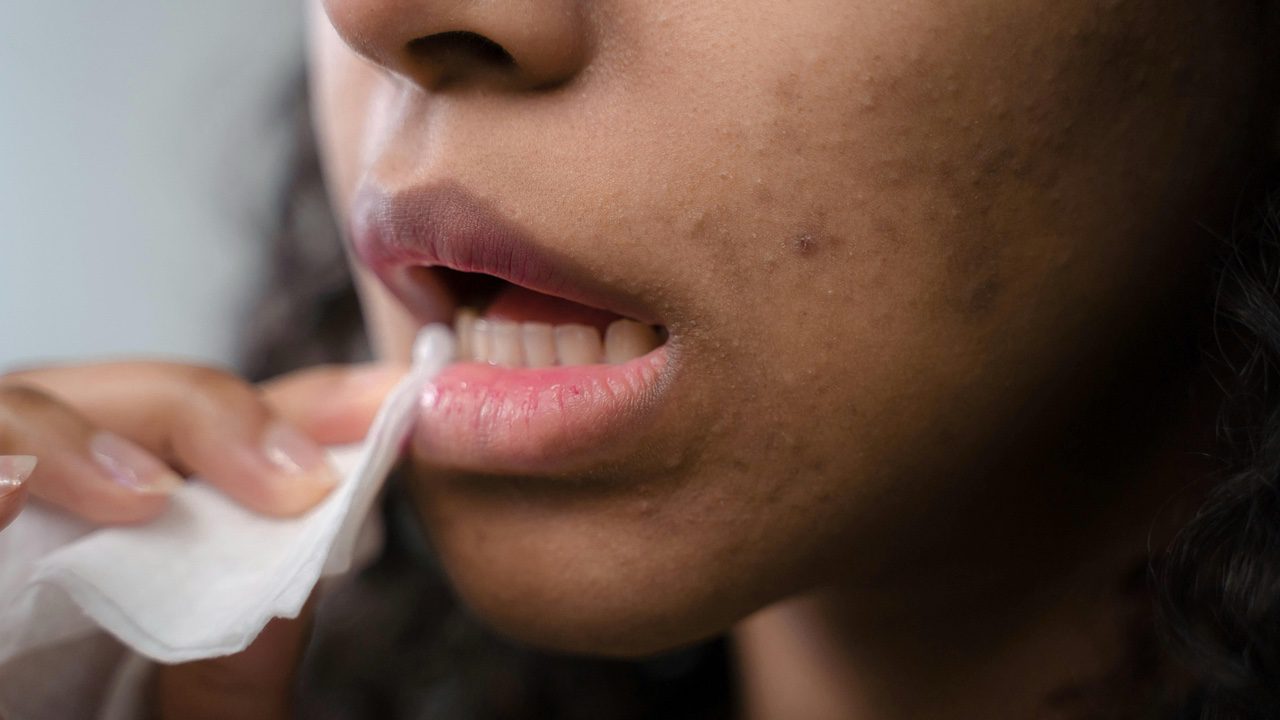 Woman wiping and cleaning makeup off mouth during beauty routine