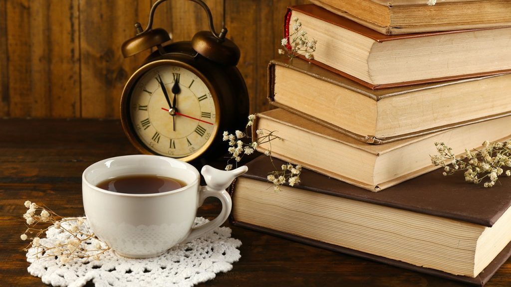 A cup of tea on a white lace doily Next to a stack of books and an old clock
