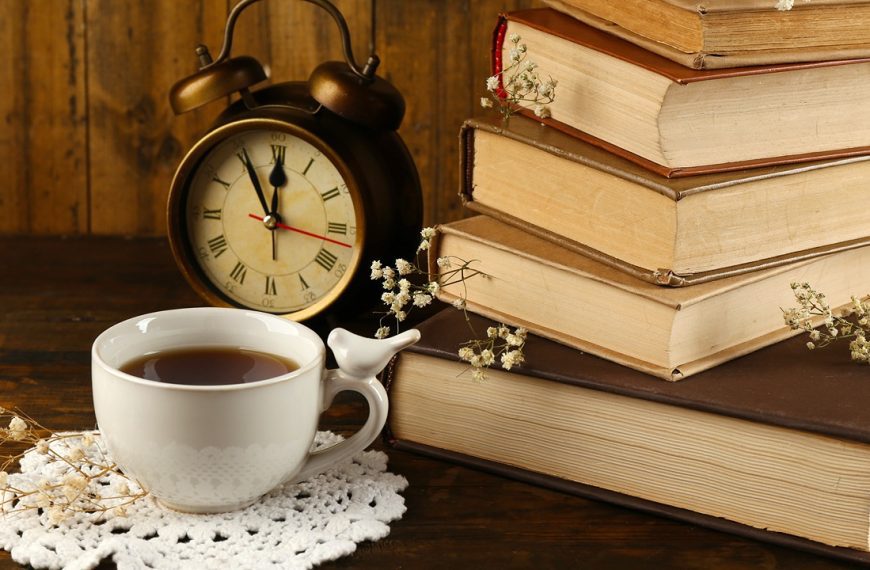 A cup of tea on a white lace doily Next to a stack of books and an old clock