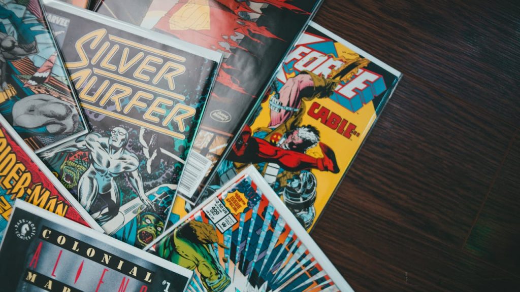 Assorted comic books on a wooden surface, featuring titles like Silver Surfer, X-Force with Cable, Spider-Man, Colonial Marines, colorful covers, some in protective plastic sleeves