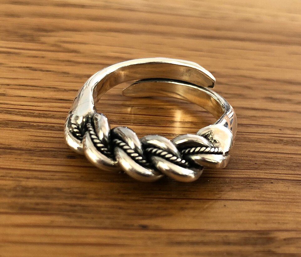 Silver adjustable ring, braided rope design, oxidized detailing for contrast, placed on a wooden surface, rustic and handcrafted appearance