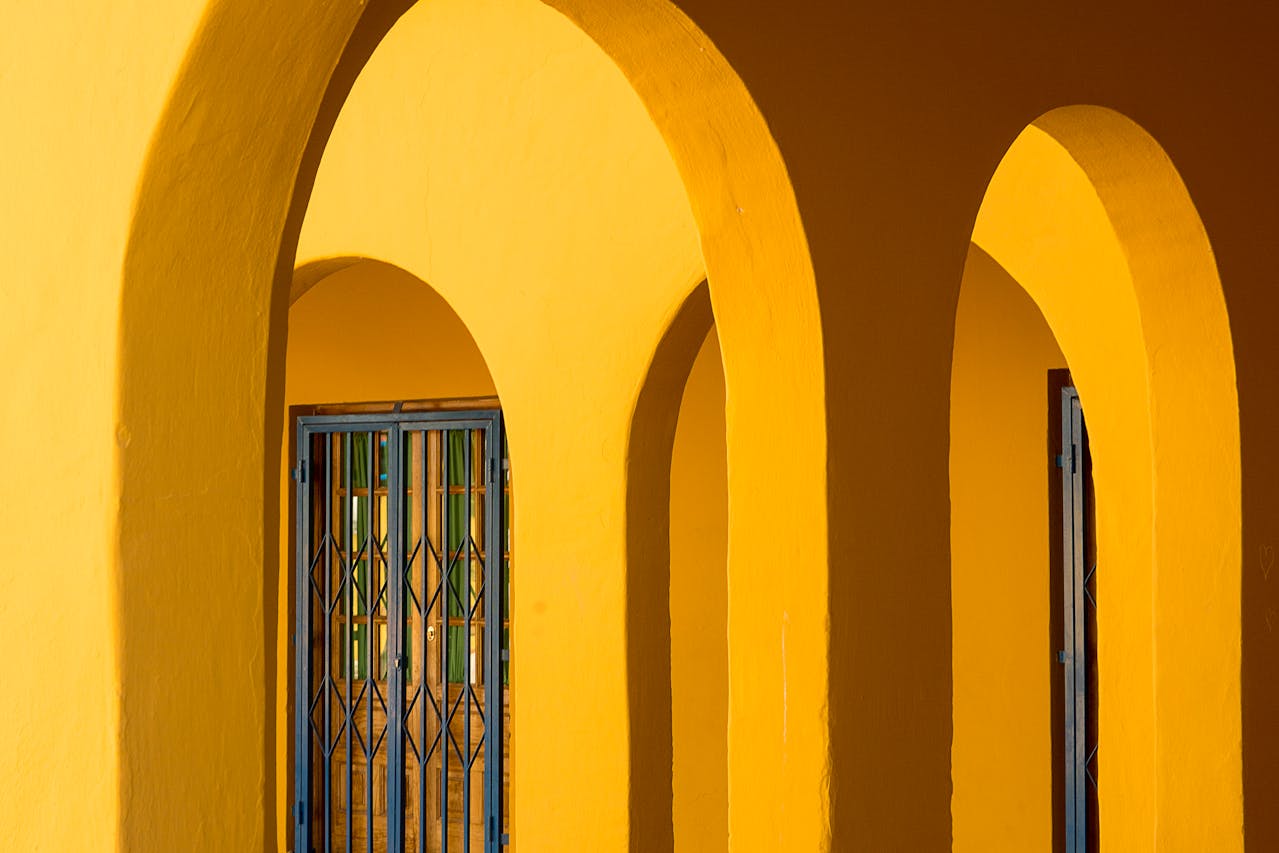 Bright yellow architectural arches, casting soft shadows, patterned glass windows in the background, warm natural lighting, vibrant Mediterranean or Spanish-style design