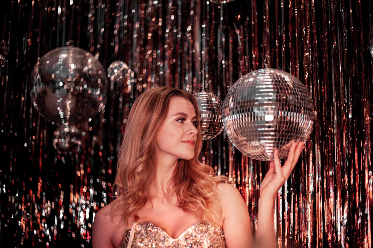 woman in sparkly dress posing with disco ball, glittery backdrop, shimmering strands, festive and glamorous atmosphere