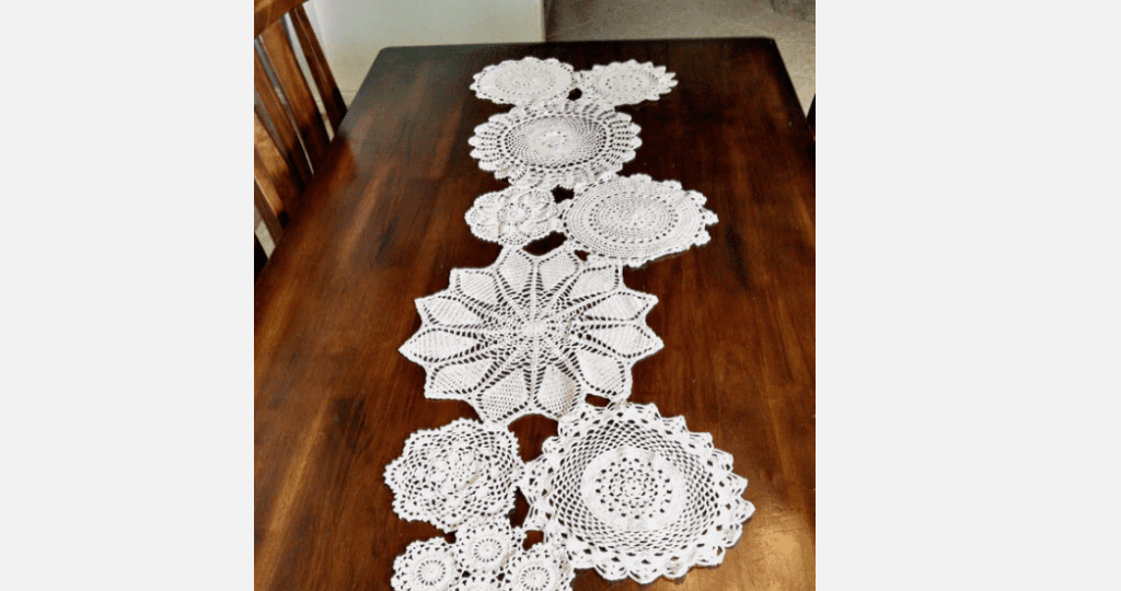 White crocheted lace table runner, floral and circular patterns, placed on a dark wooden table, handmade design, intricate threadwork, vintage or rustic home decor