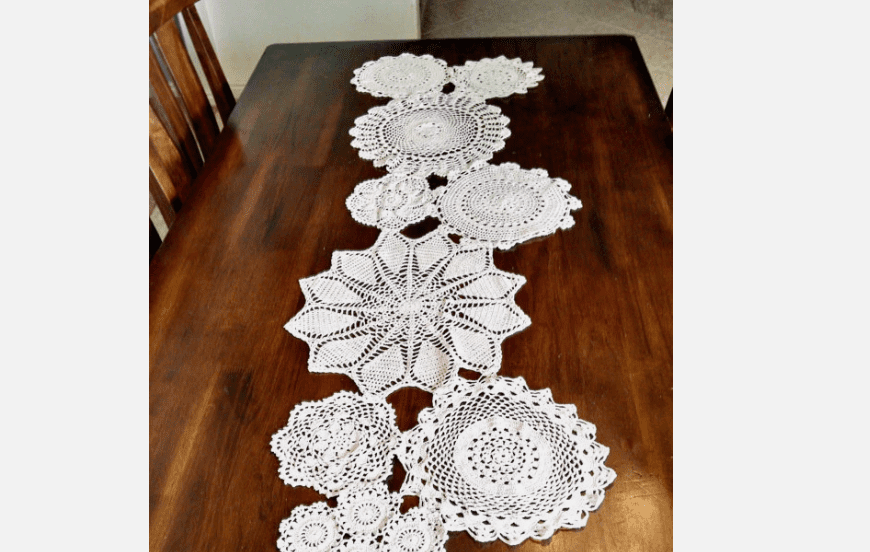White crocheted lace table runner, floral and circular patterns, placed on a dark wooden table, handmade design, intricate threadwork, vintage or rustic home decor