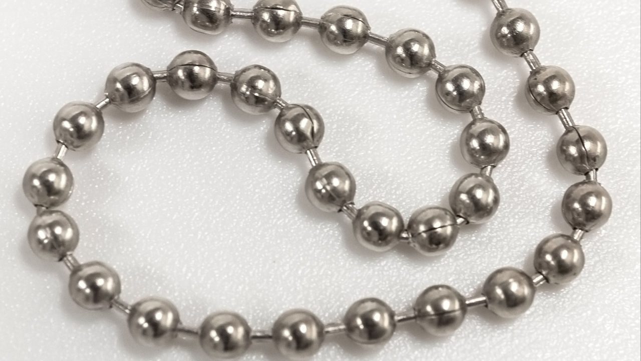 Close-up of a polished stainless steel ball chain with interconnected spherical beads on a white textured background