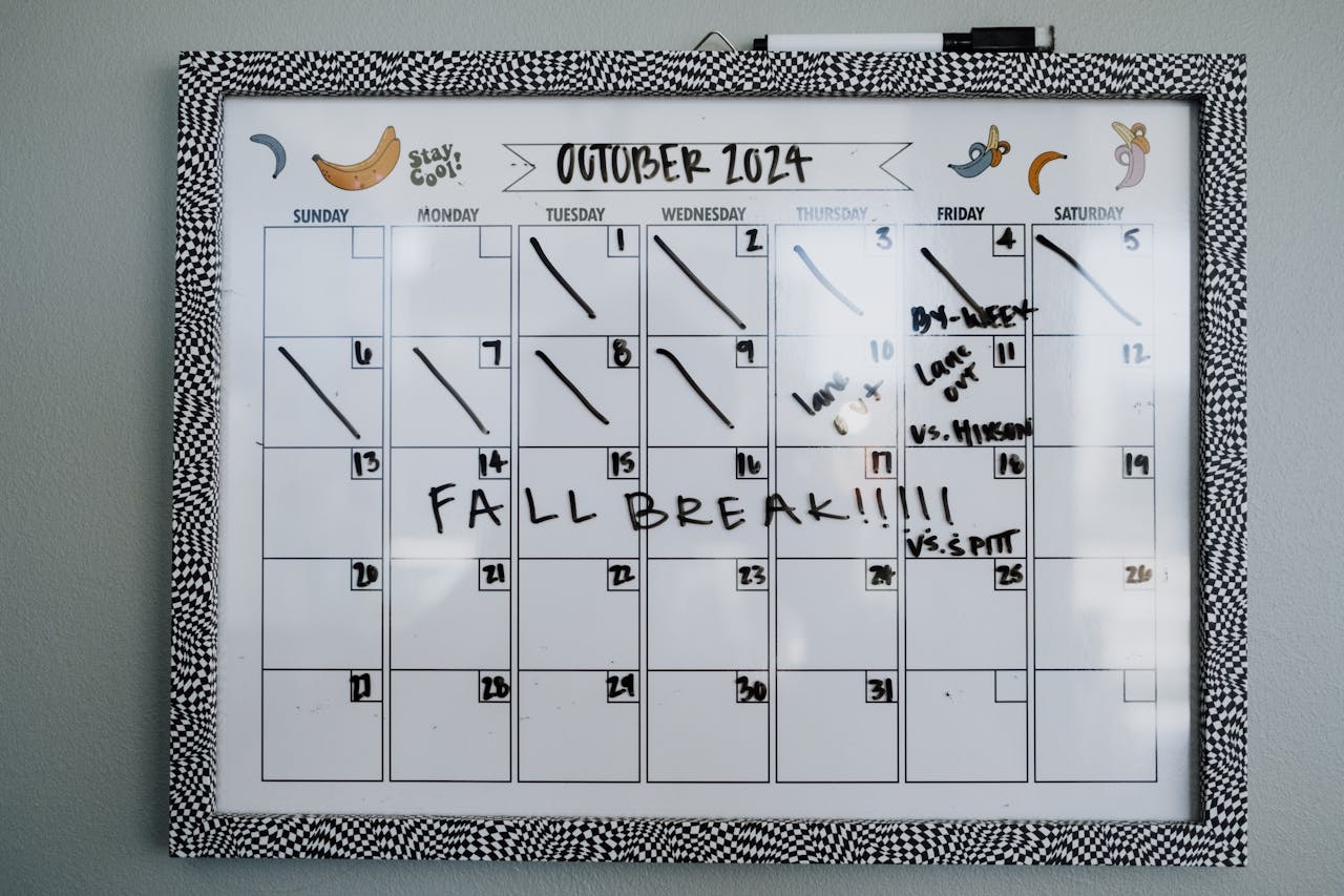 Dry erase wall calendar for October 2024 with decorative black and white checkered frame, handwritten notes, and fall break announcement