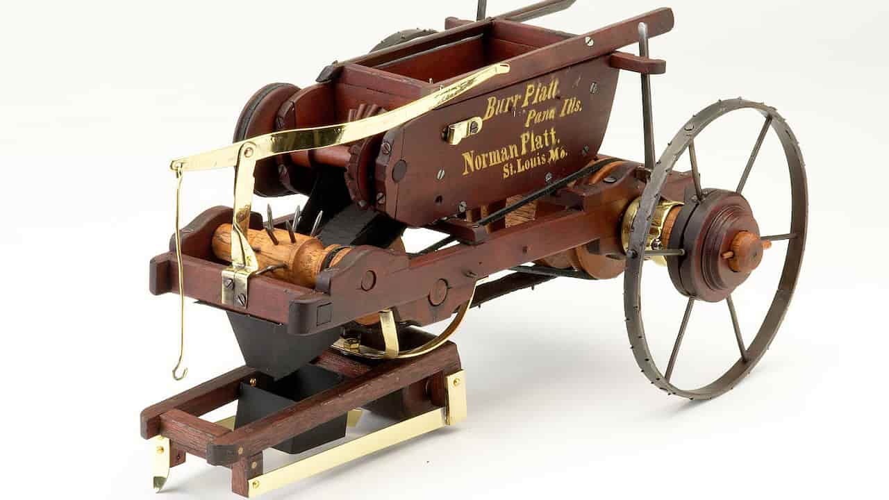 Antique wooden and metal seed planter with spoked wheels, labeled “Burr Platt Pana Ills. Norman Platt St. Louis Mo.,” featuring gears, levers, and seed compartments