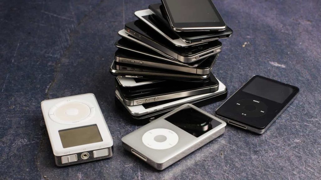 Stack of old iPods and MP3 players in black, silver, and white colors on a dark surface