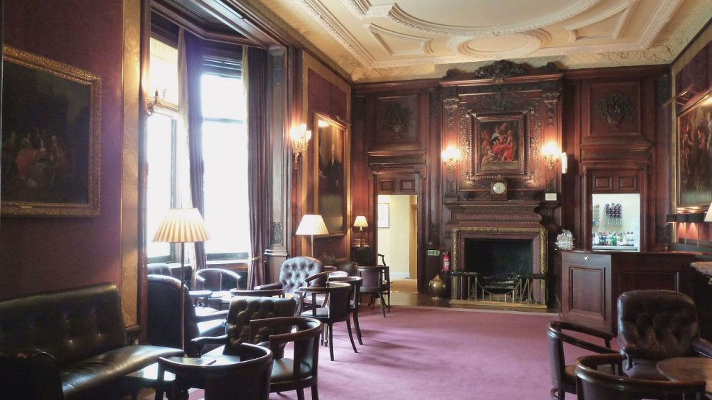 Elegant lounge with dark wood paneling, leather armchairs, classic paintings, and soft lighting in a traditional club setting