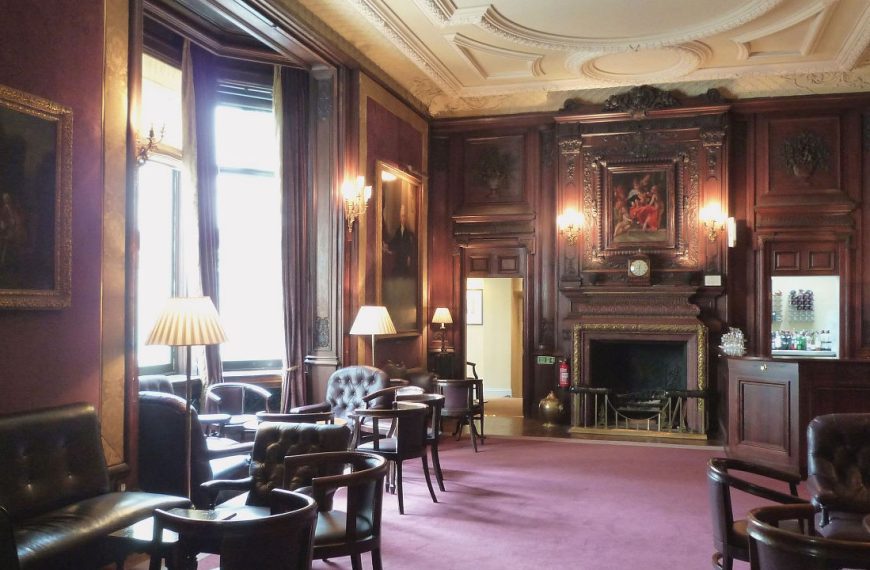 Elegant lounge with dark wood paneling, leather armchairs, classic paintings, and soft lighting in a traditional club setting