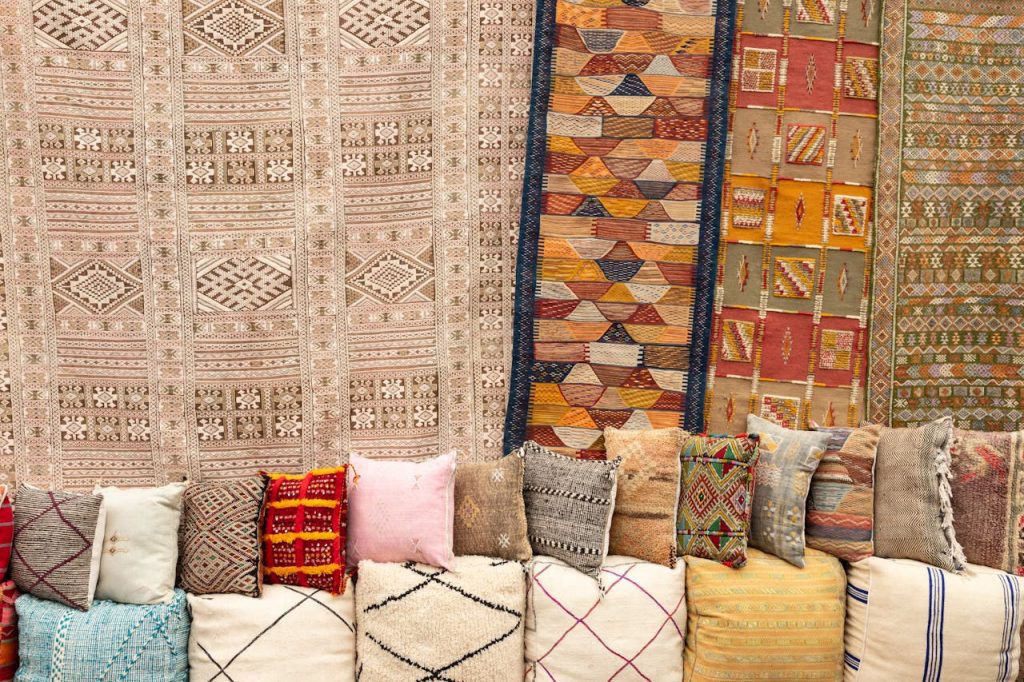 Vibrant Moroccan-inspired display with colorful woven rugs hanging on the wall, assorted textured pillows in earthy tones