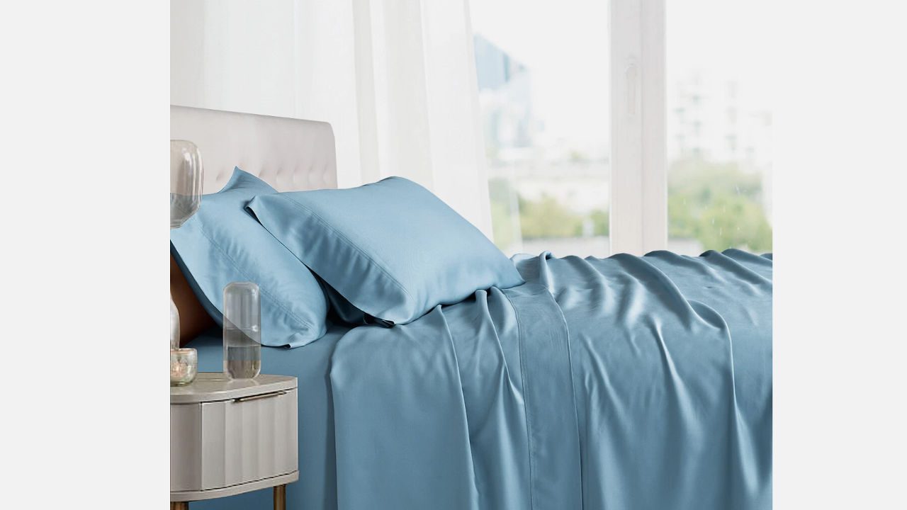 Light blue Ettitude bamboo sheet set with matching pillowcases on a modern bed beside a nightstand and window