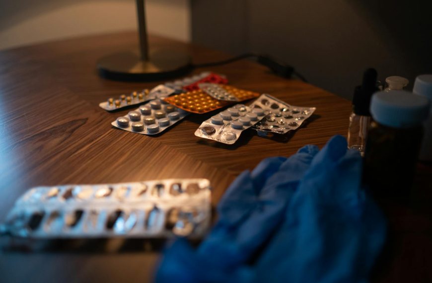 Assorted blister packs of medication and a pair of blue medical gloves on a wooden table