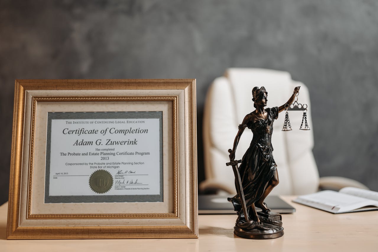 Framed law degree certificate, Lady Justice statue,grey background wall, lawyer’s office desk setup, legal profession symbolism