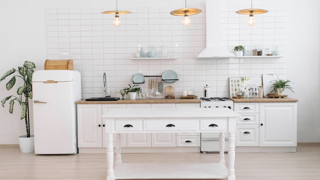 intage-style white refrigerator, curved edges, top freezer compartment, gold handle accents, positioned in a modern white kitchen, beside a potted plant, minimalist and retro design