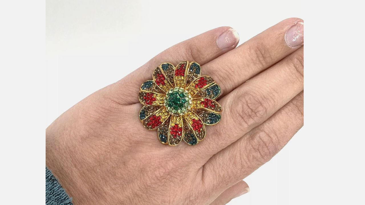 Large gold flower-shaped costume ring with red, green, yellow, and blue rhinestones worn on a person's hand