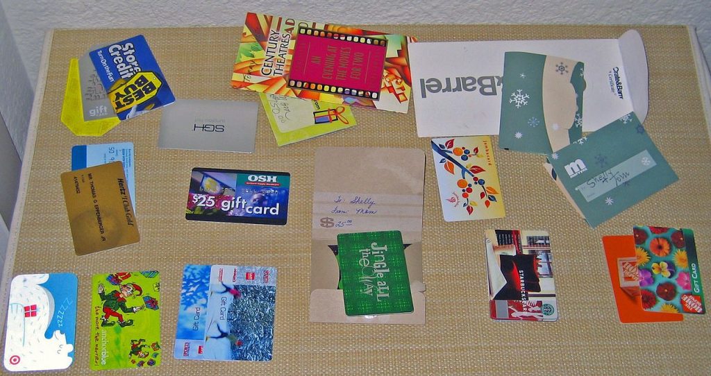 Assorted gift cards and membership cards, various brands and stores, scattered on a woven surface, colorful designs, rectangular shapes