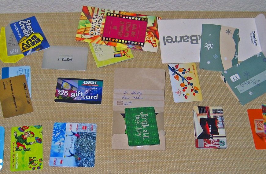 Assorted gift cards and membership cards, various brands and stores, scattered on a woven surface, colorful designs, rectangular shapes