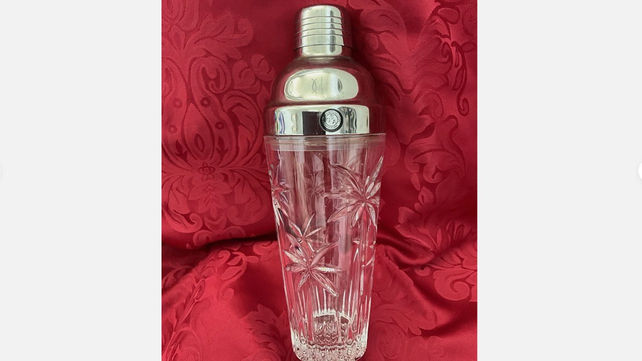 Vintage glass cocktail shaker with etched starburst design and chrome top, displayed against a red damask fabric