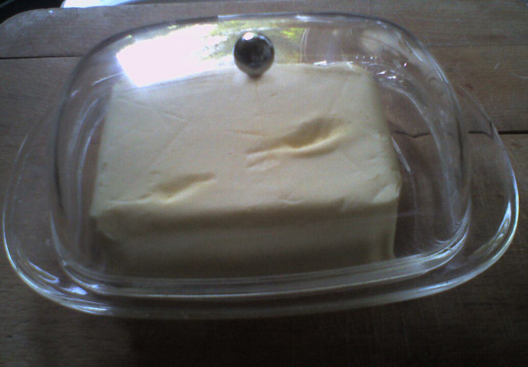 Block of butter, placed in a transparent glass container, slight indentations on the surface, wooden table background