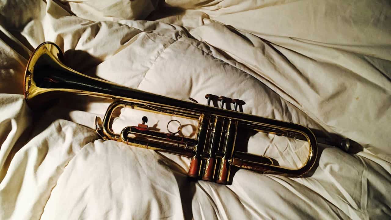A well-used brass trumpet with visible patina and red valve caps resting on a white quilted blanket