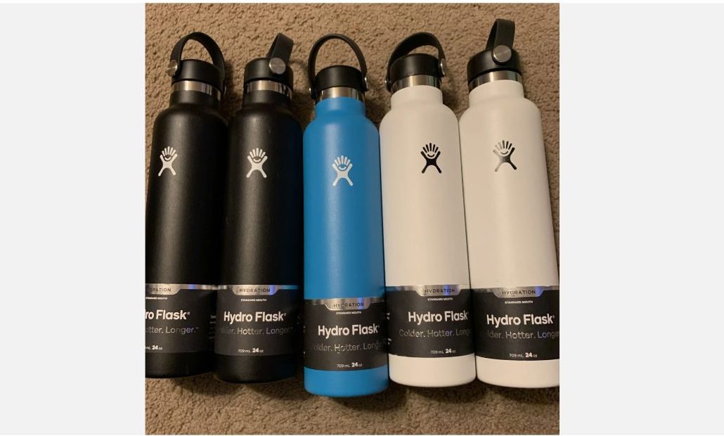 Five Hydro Flask water bottles in black, blue, and white, with flip-top lids, arranged side by side