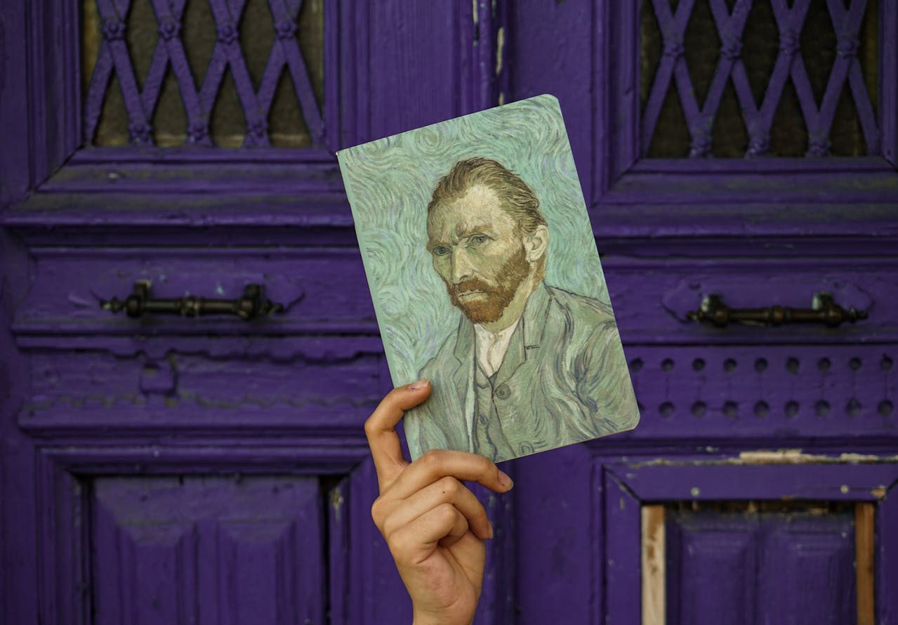 Hand holding a notebook with a Vincent van Gogh portrait cover in front of a vintage purple wooden door