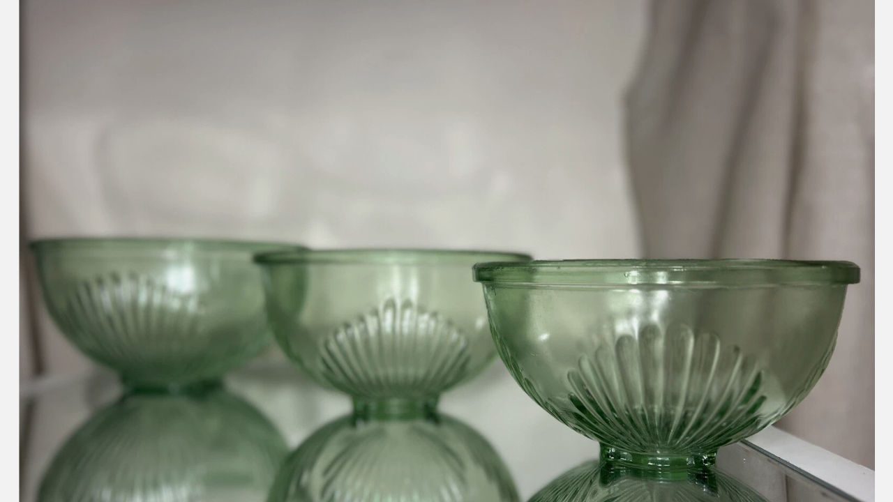 Three vintage green glass mixing bowls with ribbed detailing, displayed in a row on a reflective surface