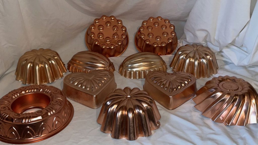 Collection of vintage copper and aluminum Jell-O molds in various shapes including hearts, rounds, and fluted designs