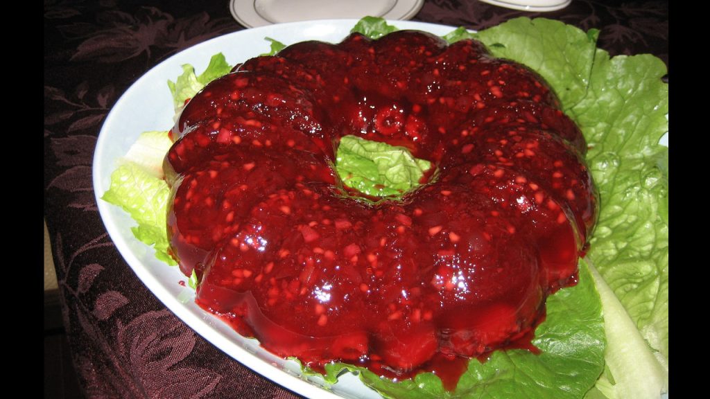 Vintage cranberry Jell-O salad mold with fruit and nuts, served on a bed of lettuce on a white platter