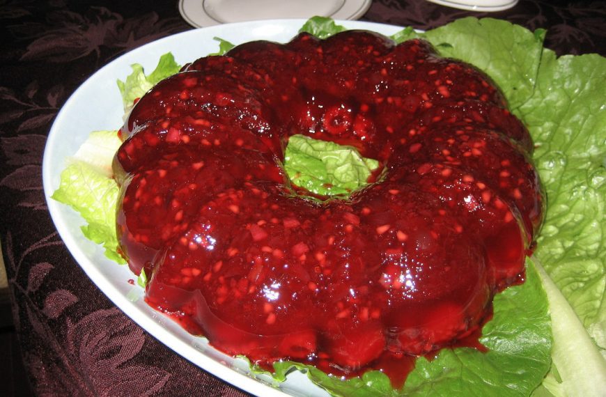 Vintage cranberry Jell-O salad mold with fruit and nuts, served on a bed of lettuce on a white platter
