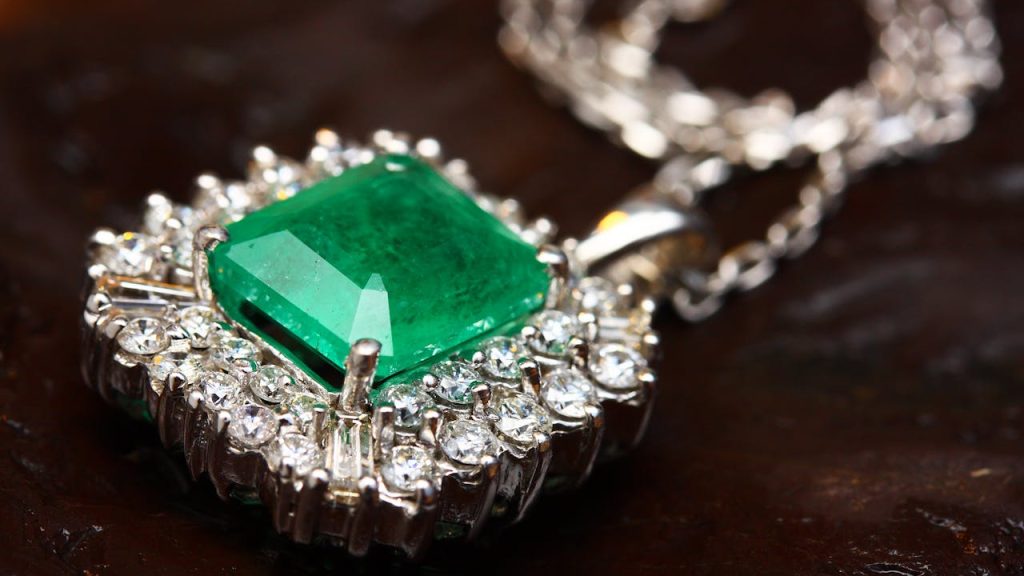 Elegant necklace with a large emerald-cut green gemstone, surrounded by a halo of clear diamonds, set in a silver or white gold frame