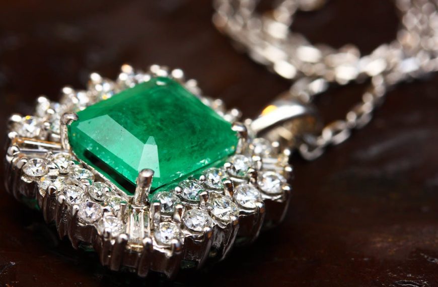 Elegant necklace with a large emerald-cut green gemstone, surrounded by a halo of clear diamonds, set in a silver or white gold frame