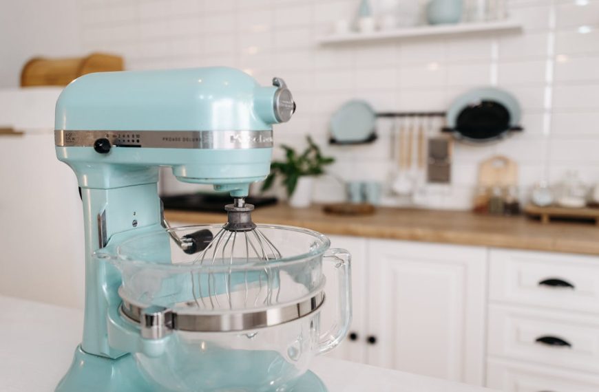 Light blue KitchenAid stand mixer with a clear glass mixing bowl on a white kitchen counter