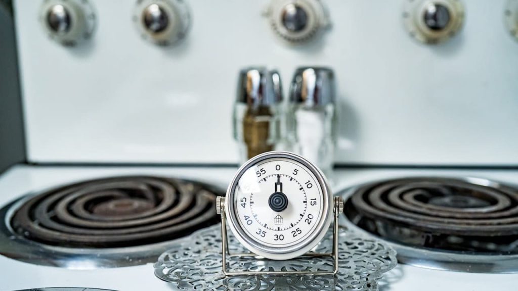 Kitchen timer set on a stove, vintage electric stovetop with coil burners, salt and pepper shakers in the background, retro-style appliance knobs