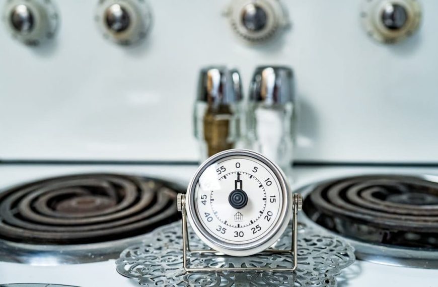 Kitchen timer set on a stove, vintage electric stovetop with coil burners, salt and pepper shakers in the background, retro-style appliance knobs