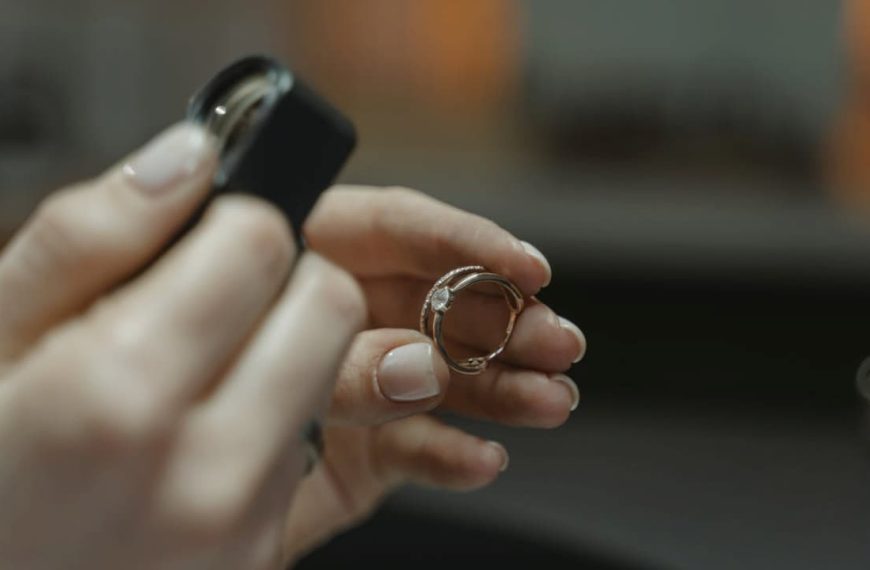 Hands inspecting a gold ring with a jeweler’s loupe, close-up view, focus on detailed examination, soft lighting, neutral background, ring held between fingers, tool used to check markings or authenticity