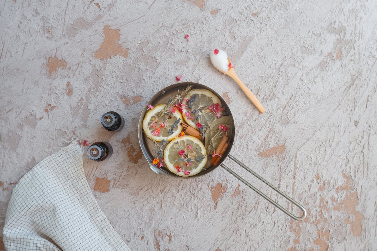 Metal pot filled with lemon slices, rosemary, and other herbs, simmering ingredients arranged on a textured countertop, natural potpourri setup