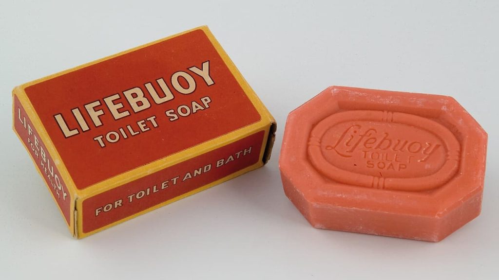 Vintage Lifebuoy toilet soap with its original packaging. A coral-pink octagonal bar with embossed "Lifebuoy Toilet Soap" logo sits beside its red and yellow box labeled "LIFEBUOY TOILET SOAP" and FOR TOILET AND BATH