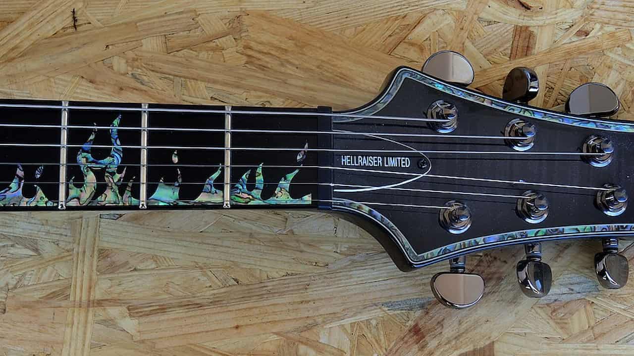 Close-up of the headstock and upper neck of a limited edition electric guitar labeled “HELLRAISER LIMITED,” featuring abalone flame inlays on a dark fretboard and chrome tuning pegs