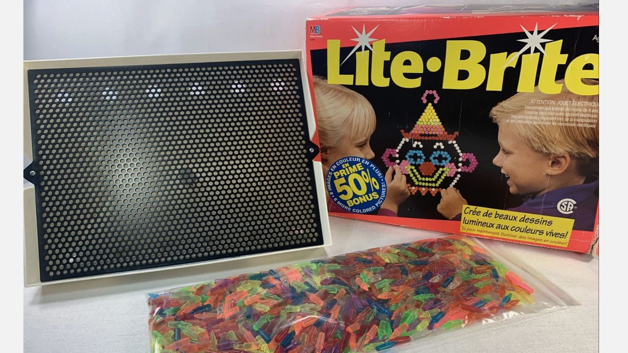 Lite-Brite toy set with black peg board, colorful translucent pegs in a bag, and original box featuring children creating a clown image