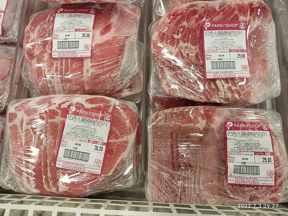 Four large cuts of raw red meat, vacuum-sealed in clear plastic, labeled with pricing and weight stickers, displayed in a refrigerated meat section