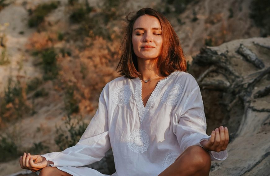 Meditation relaxing, Woman meditating outdoors, eyes closed, wearing white top, sitting calmly in natural setting, sunset light