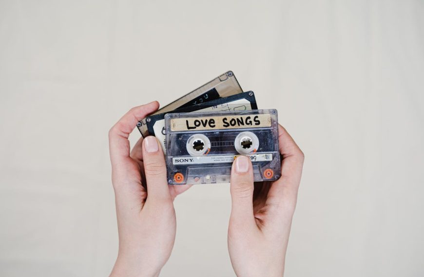 Hands holding three vintage cassette tapes against a plain light background. The front cassette has a handwritten label reading "LOVE SONGS" and is a Sony brand tape