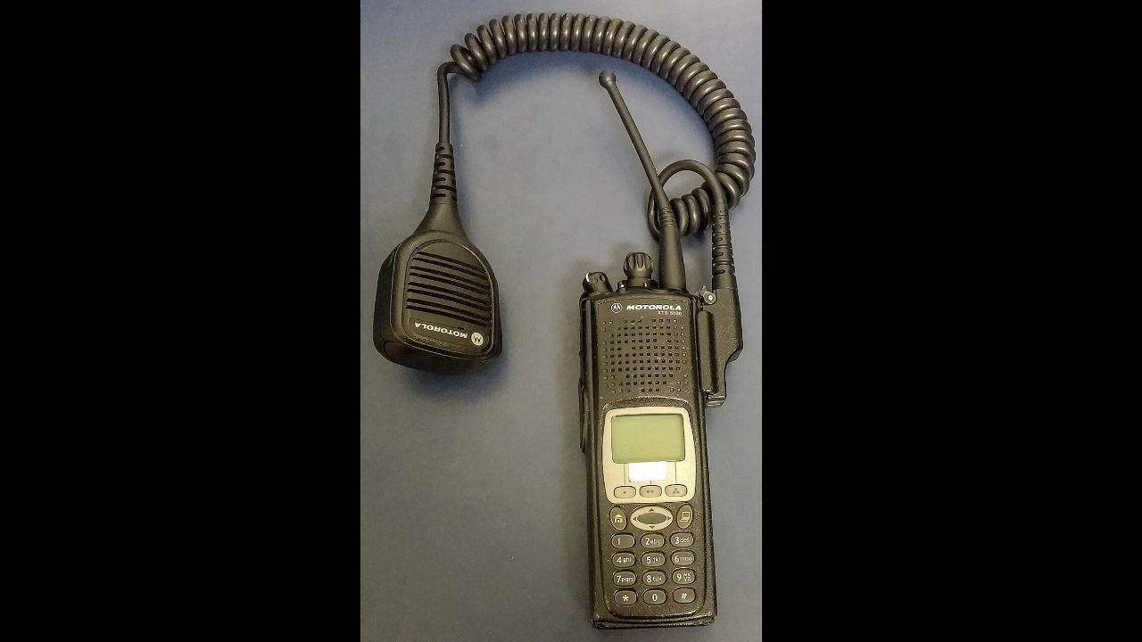 Motorola XTS/XTL 5000 two-way radio with keypad, LCD screen, and coiled remote speaker microphone attachment