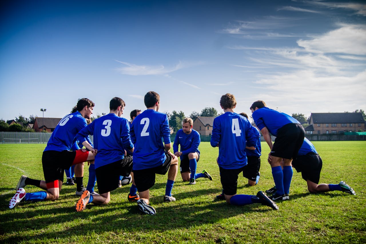 Soccer coach giving instructions to team in blue jerseys kneeling on a grassy field during practice or match