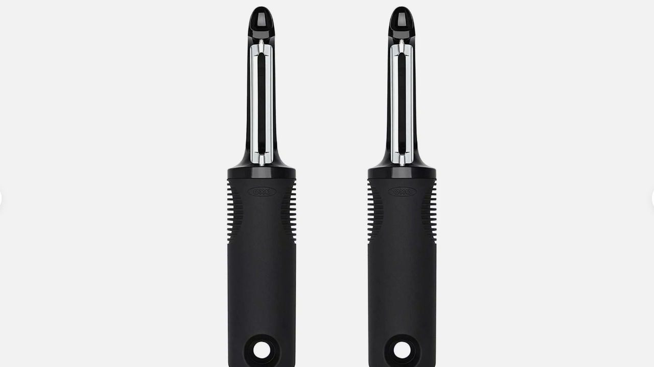 Two identical black-handled OXO Good Grips swivel peelers with stainless steel blades standing upright side by side