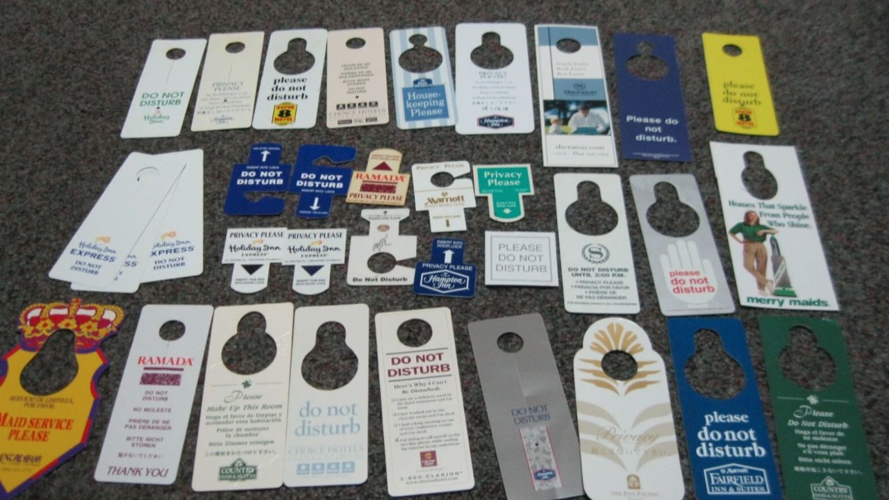 Collection of vintage and modern hotel "Do Not Disturb" door hangers in various designs, colors, and branding, arranged on a textured gray carpet